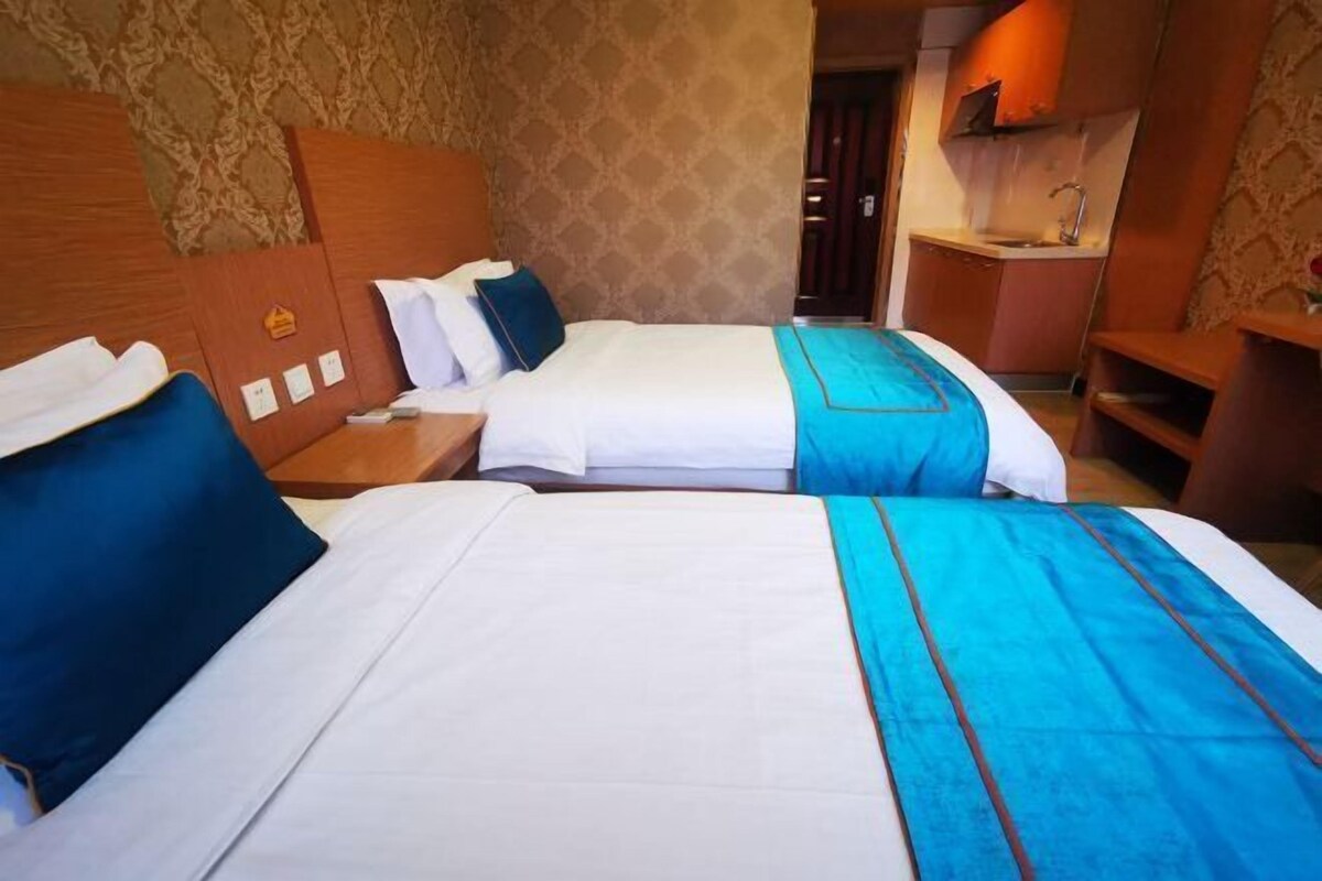 A hotel room with two beds, a small kitchenette, and a bathroom.