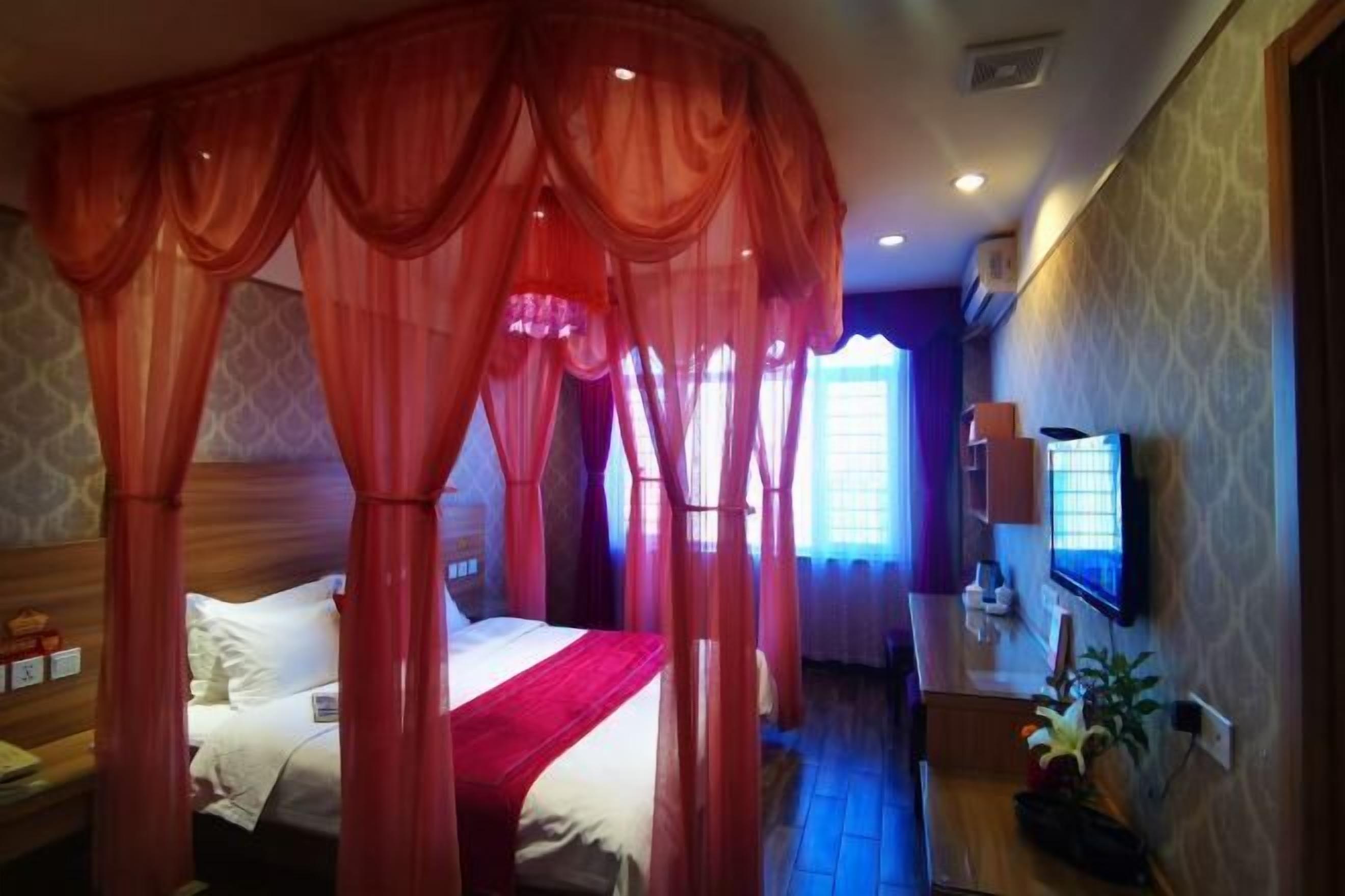 A hotel room with a canopy bed, a television, and a small desk area.