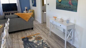 Ein Wohnzimmer mit einer Couch, einem Fernseher, einem Vogelgemälde und einem Tisch mit einer Flasche.
