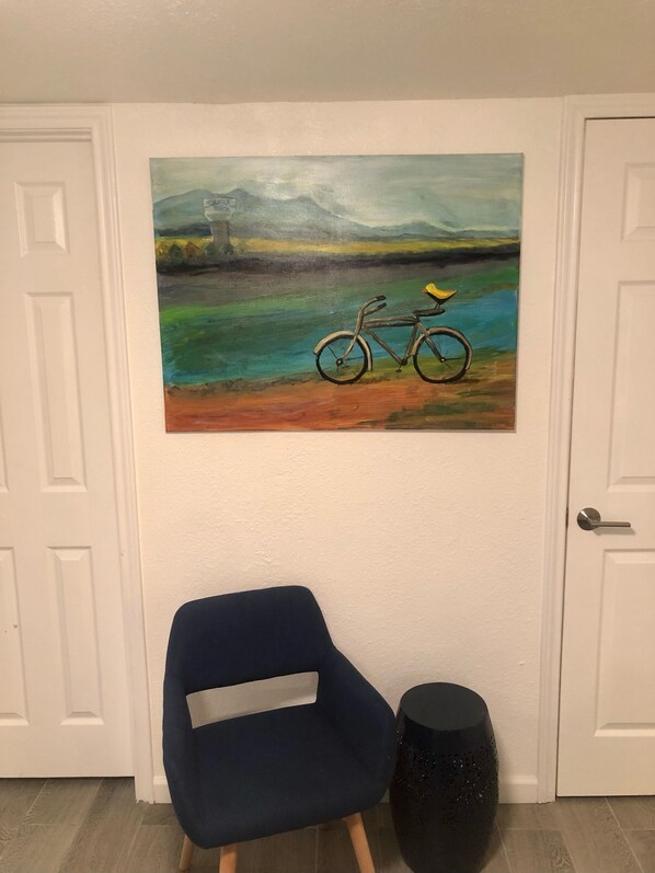 A room with a blue chair, a black round table, and a painting of a bicycle on the wall.