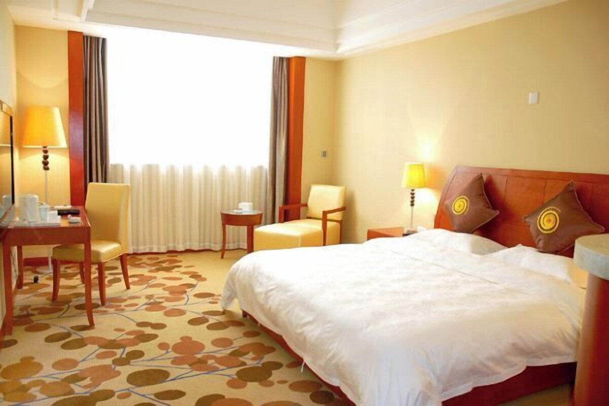 A hotel room with a large bed, two chairs, a small table, and a desk.