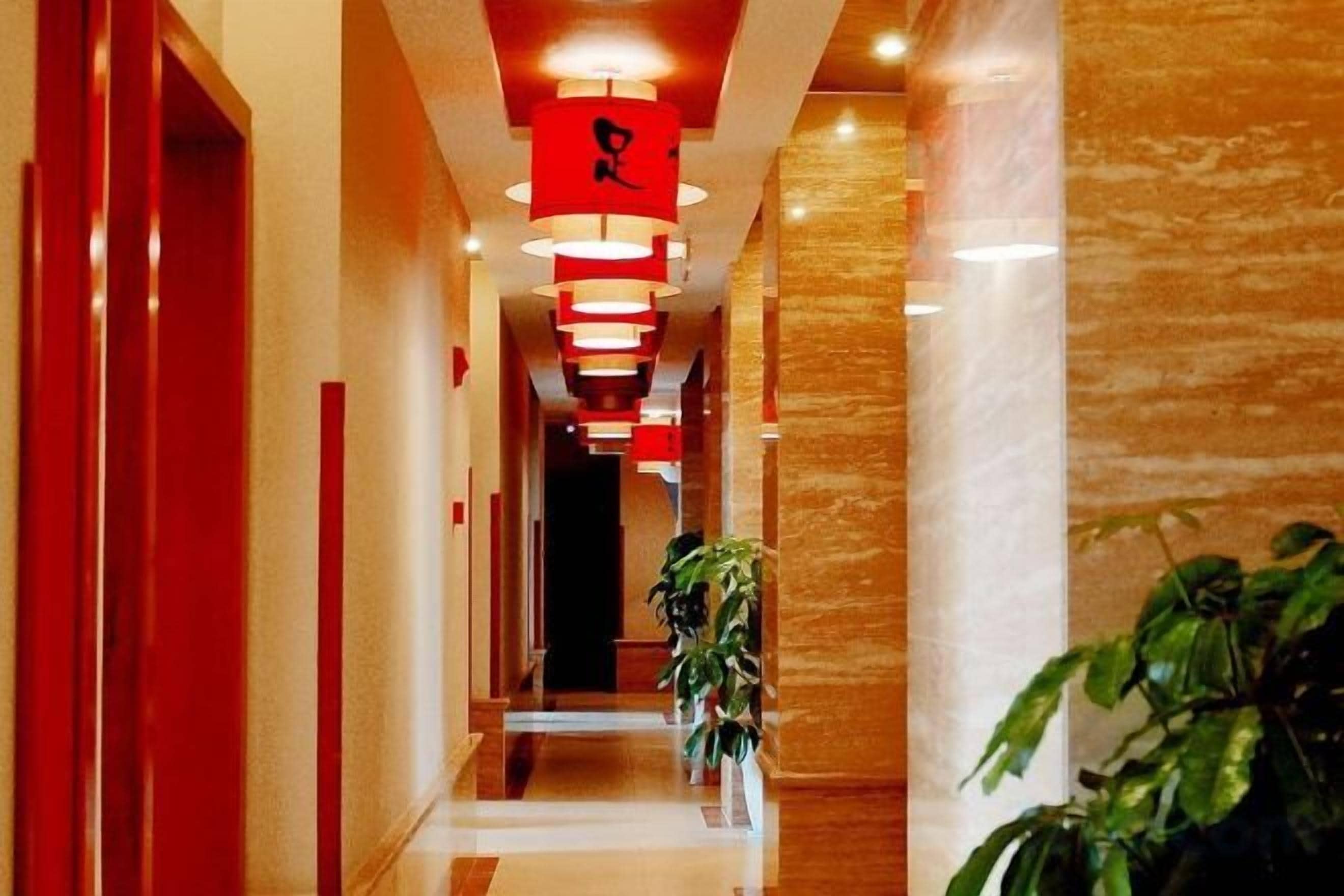 A corridor with red doors, a plant, and hanging red lights.