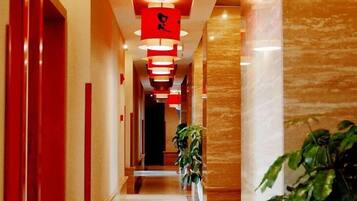 A corridor with red doors, a plant, and hanging red lights.