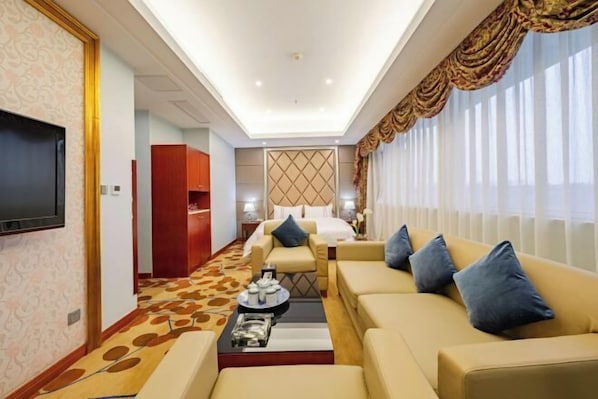 A hotel room with a large flat-screen TV, a sofa set, a coffee table, and a patterned carpet.