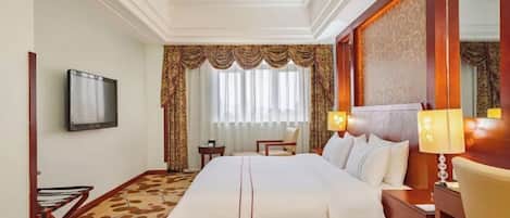 A hotel room with a large bed, a television, a desk with a lamp, and a chair.
