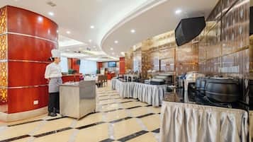 A hotel lobby with a chef at the reception, a buffet setup, and a large screen.