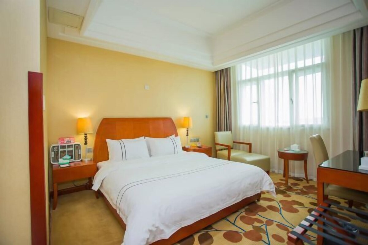 A hotel room with a large bed, bedside tables, a chair, a desk, and a window with curtains.