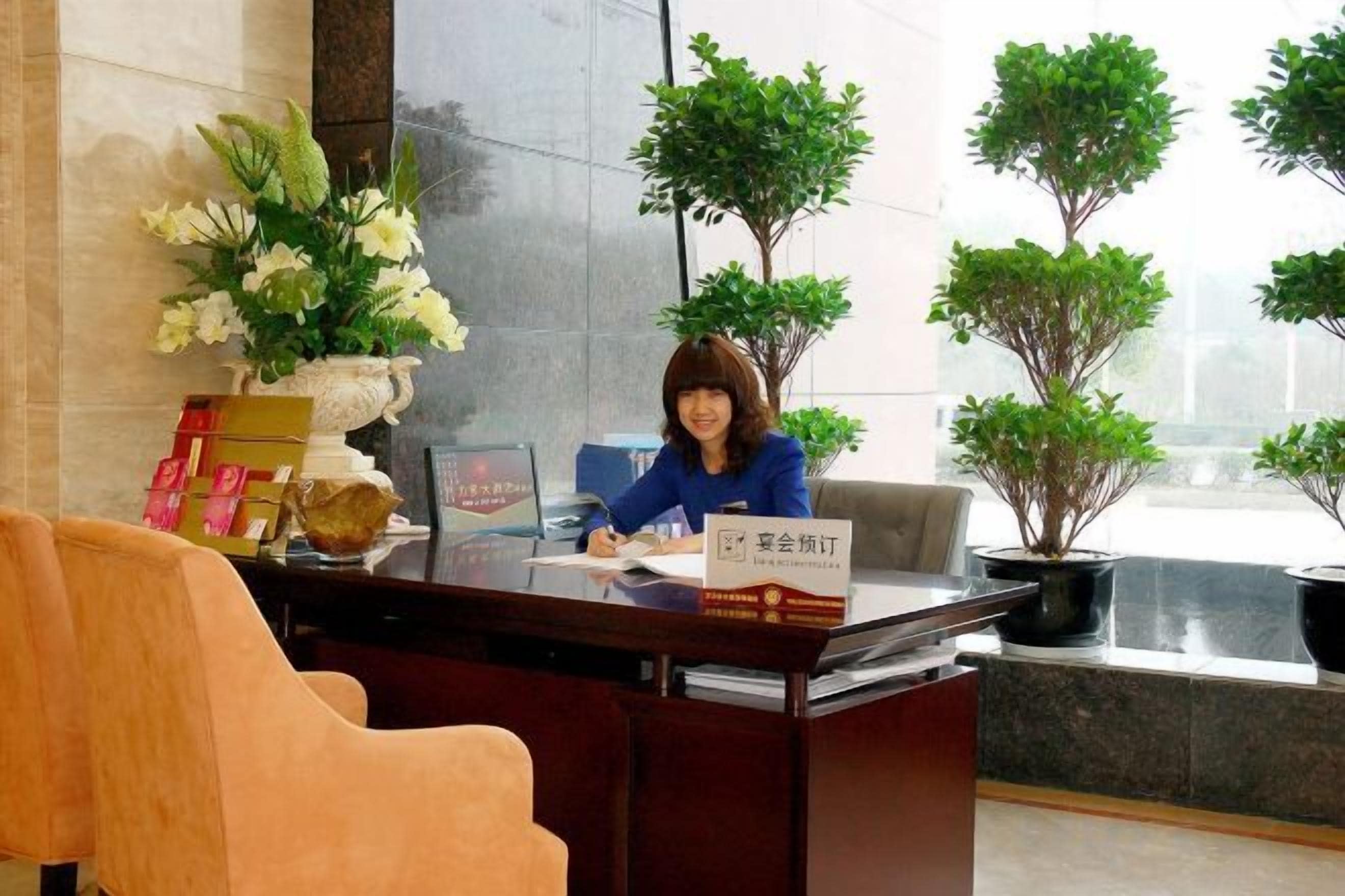 A reception desk with a nameplate, a potted plant, and a vase with flowers.