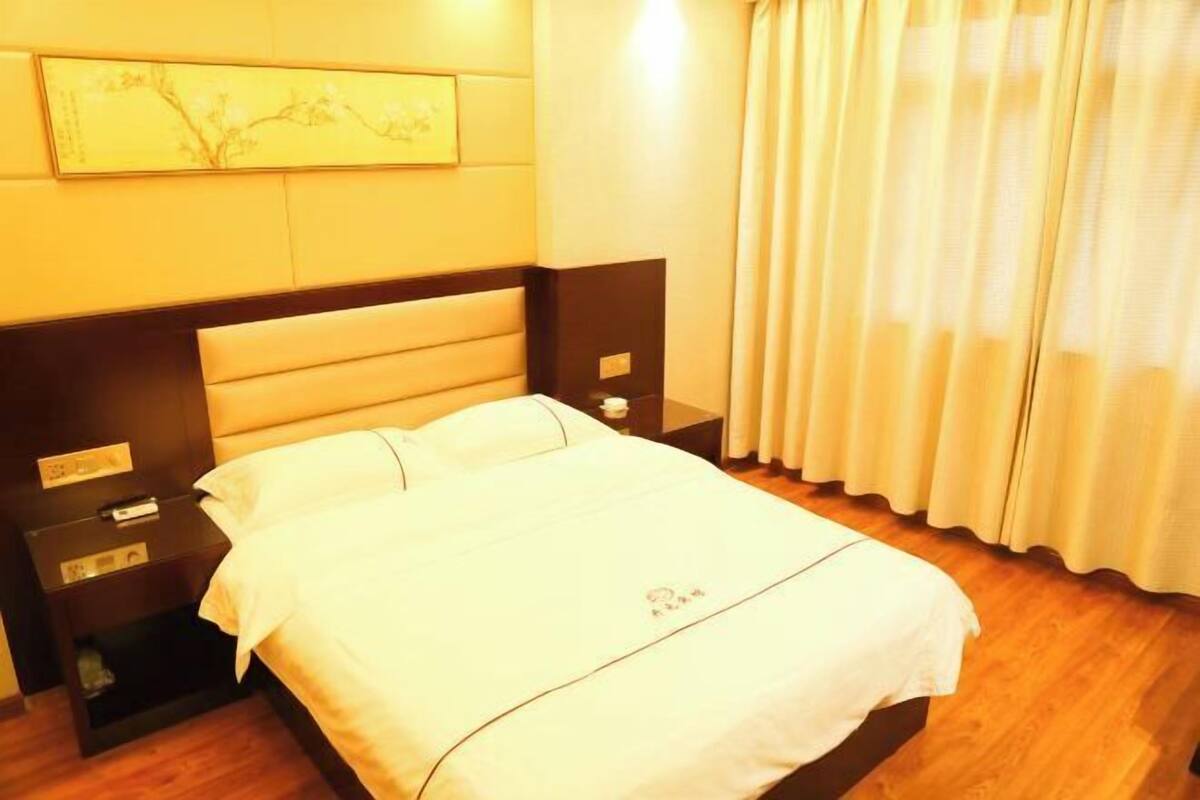 A hotel room with a bed, bedside tables, a nightstand, a wall-mounted artwork, and a window with curtains.
