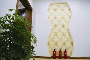 A wall with a patterned wallpaper, a potted plant, and three fire extinguishers.