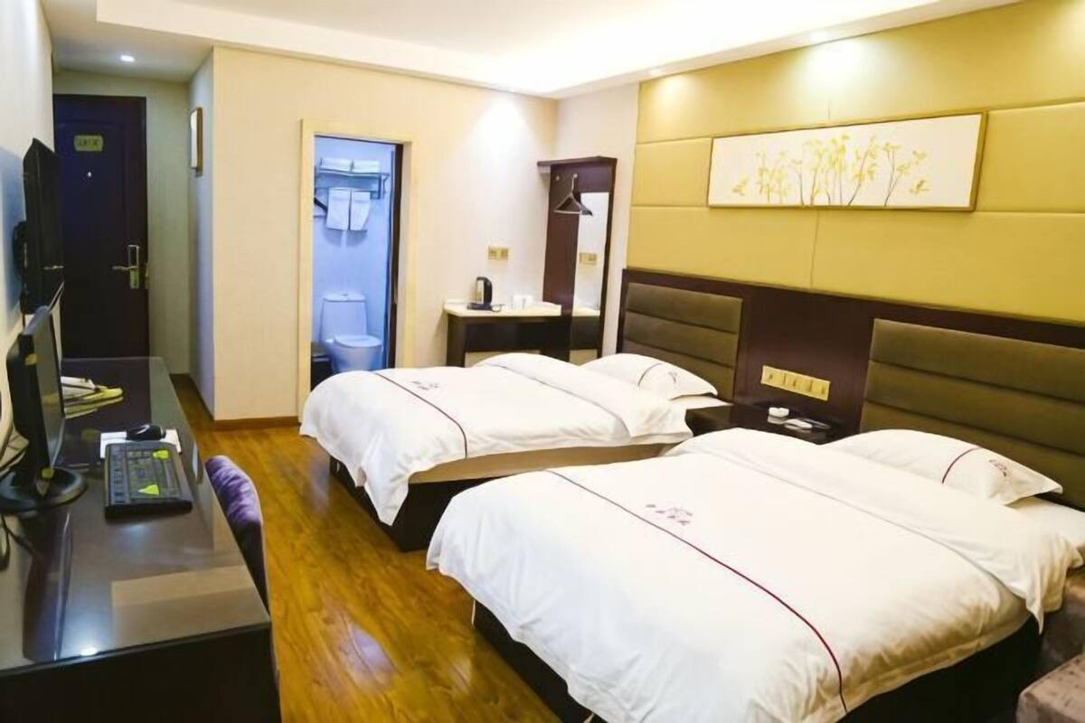 A hotel room with two beds, a desk with a computer, a mirror, and a painting on the wall.