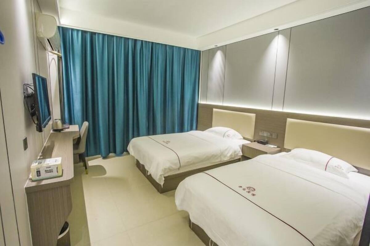 A hotel room with two beds, a desk with a computer, and a blue curtain.