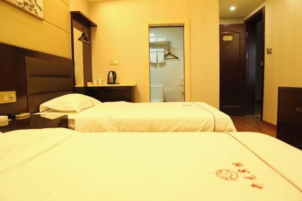 A hotel room with two beds, a bedside table, a mirror, a wardrobe, and a door leading to a bathroom.