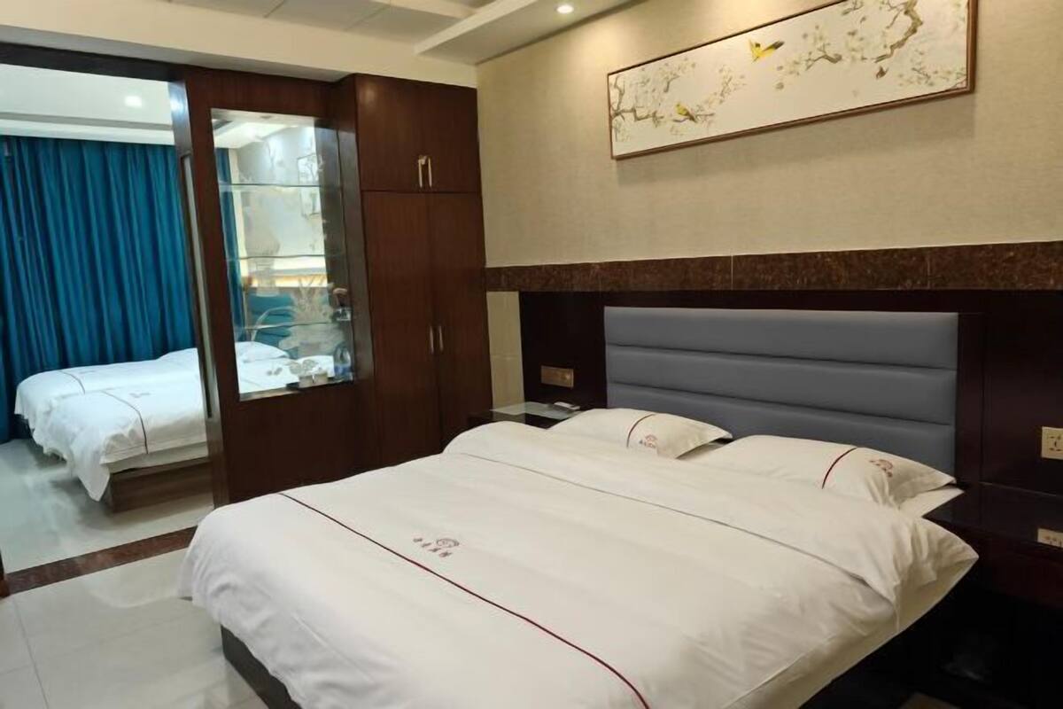 A hotel room with a large bed, a wardrobe, a mirror, and a painting on the wall.