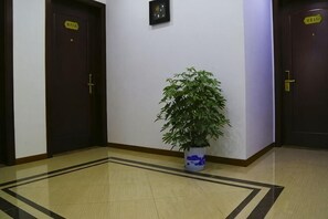 A hallway with a potted plant, two doors with signs, and a patterned floor.