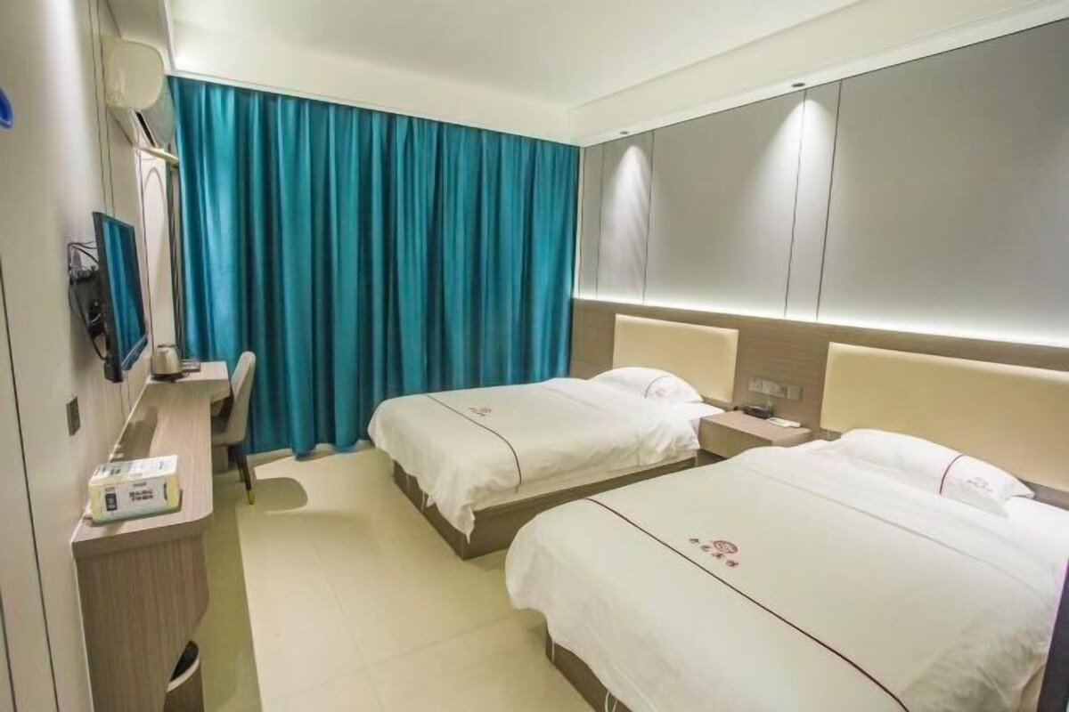 A hotel room with two beds, a desk, a chair, and a TV.
