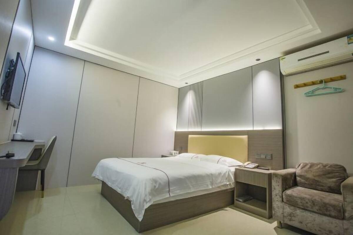 A modern hotel room with a bed, bedside table, chair, and a TV mounted on the wall.