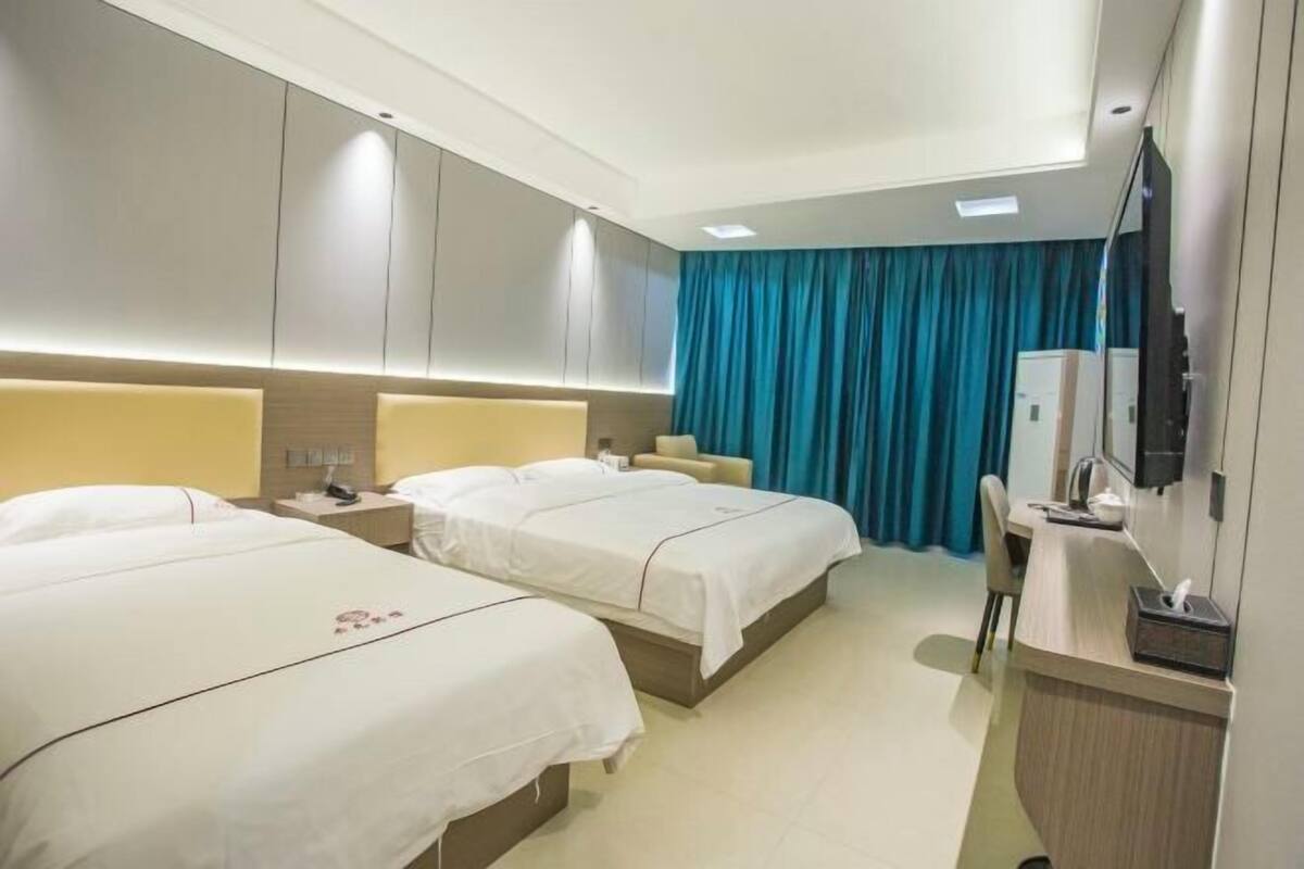 A hotel room with two beds, a desk with a computer, a TV, and a minibar.