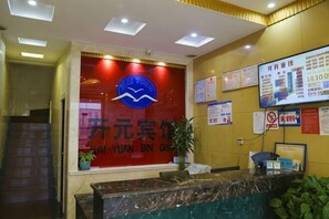 A reception area with a red wall, a reception desk, a potted plant, and various informational posters.