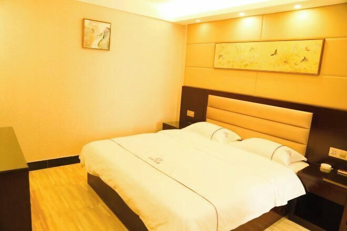 A hotel room with a large bed, a headboard with a built-in shelf, a bedside table, and a wall-mounted artwork.