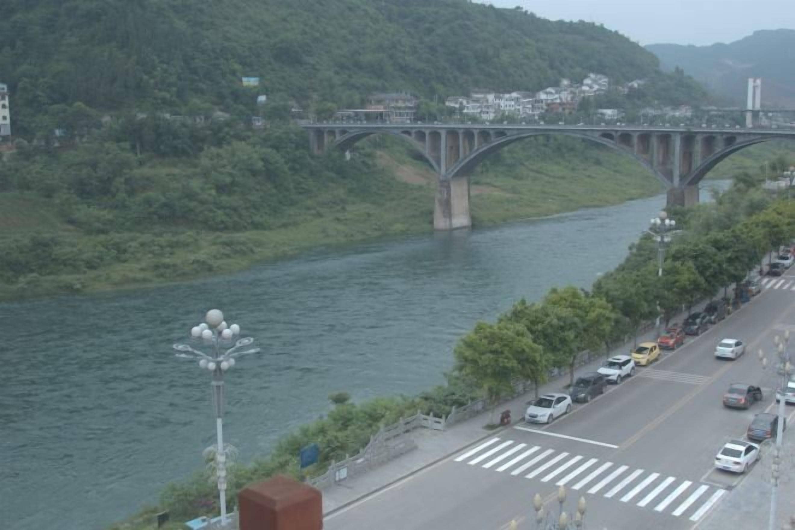 A river with a bridge, a road with cars, and greenery.