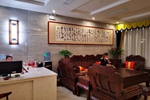 A reception area with a desk, chairs, a large calligraphy artwork, and a window with curtains. - Guihong Hotel (Zunyi)