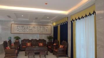 A traditional-style lobby with a large wooden table and chairs, a framed calligraphy artwork, and a large window with curtains.