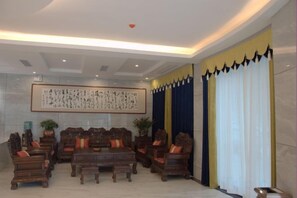 A traditional-style lobby with a large wooden table and chairs, a framed calligraphy artwork, and a large window with curtains. - Guihong Hotel (Zunyi)