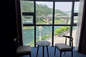 Una habitación con un ventanal grande, dos sillas, una mesita y vistas a un puente sobre un río.