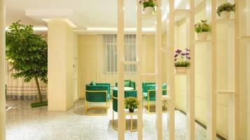 A hotel lobby with green seating, a large plant, and a decorative white partition.