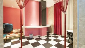 A modern bathroom with a checkered floor, a pink accent wall, and a blue sofa in the background. - Yuxi Zhuoran Xinzhuang Hotel (Yuxi)