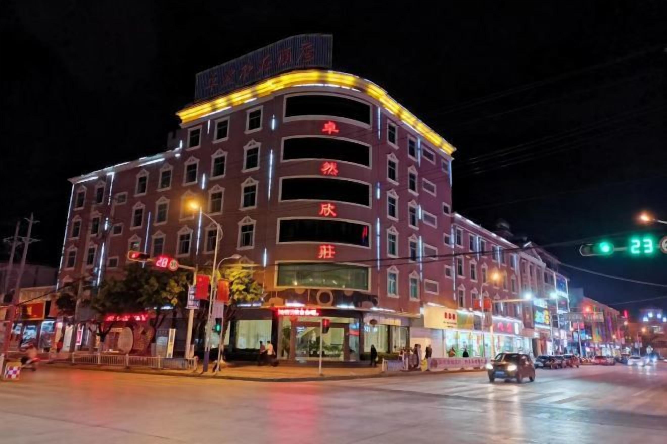 A multi-story hotel with a curved facade, illuminated signage, and a street view with a traffic light.