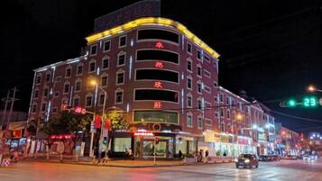 A multi-story hotel with a curved facade, illuminated signage, and a street view with a traffic light.