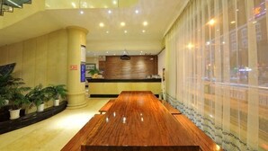 A hotel lobby with a wooden reception desk, a large pillar, potted plants, and a view through a window. - Yuxi Zhuoran Xinzhuang Hotel (Yuxi)