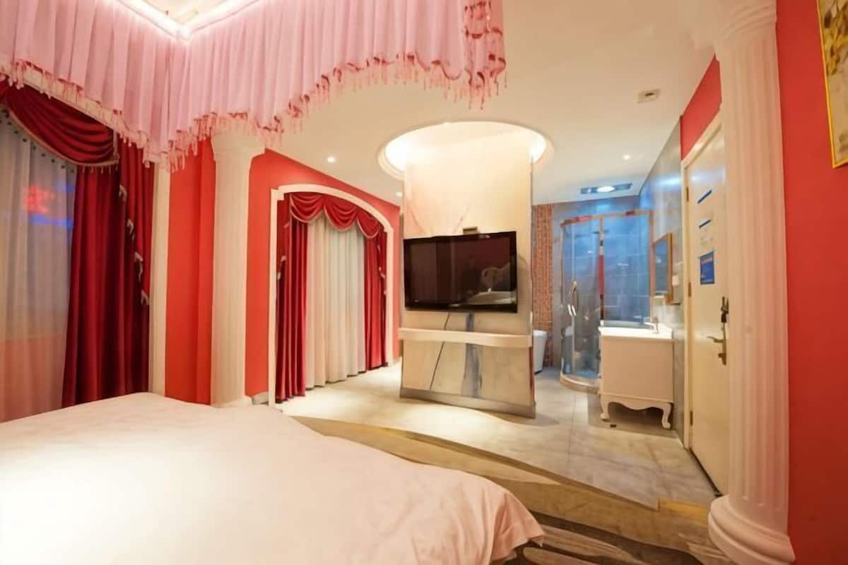 Et hotelværelse med seng, fjernsyn, badeværelse og glasvægsbruser.