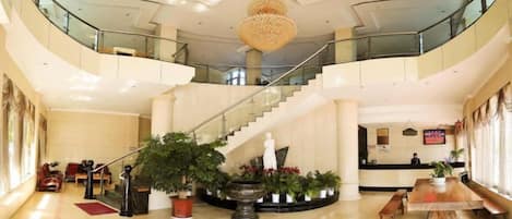 A spacious lobby with a grand staircase, a reception desk, and multiple seating areas.