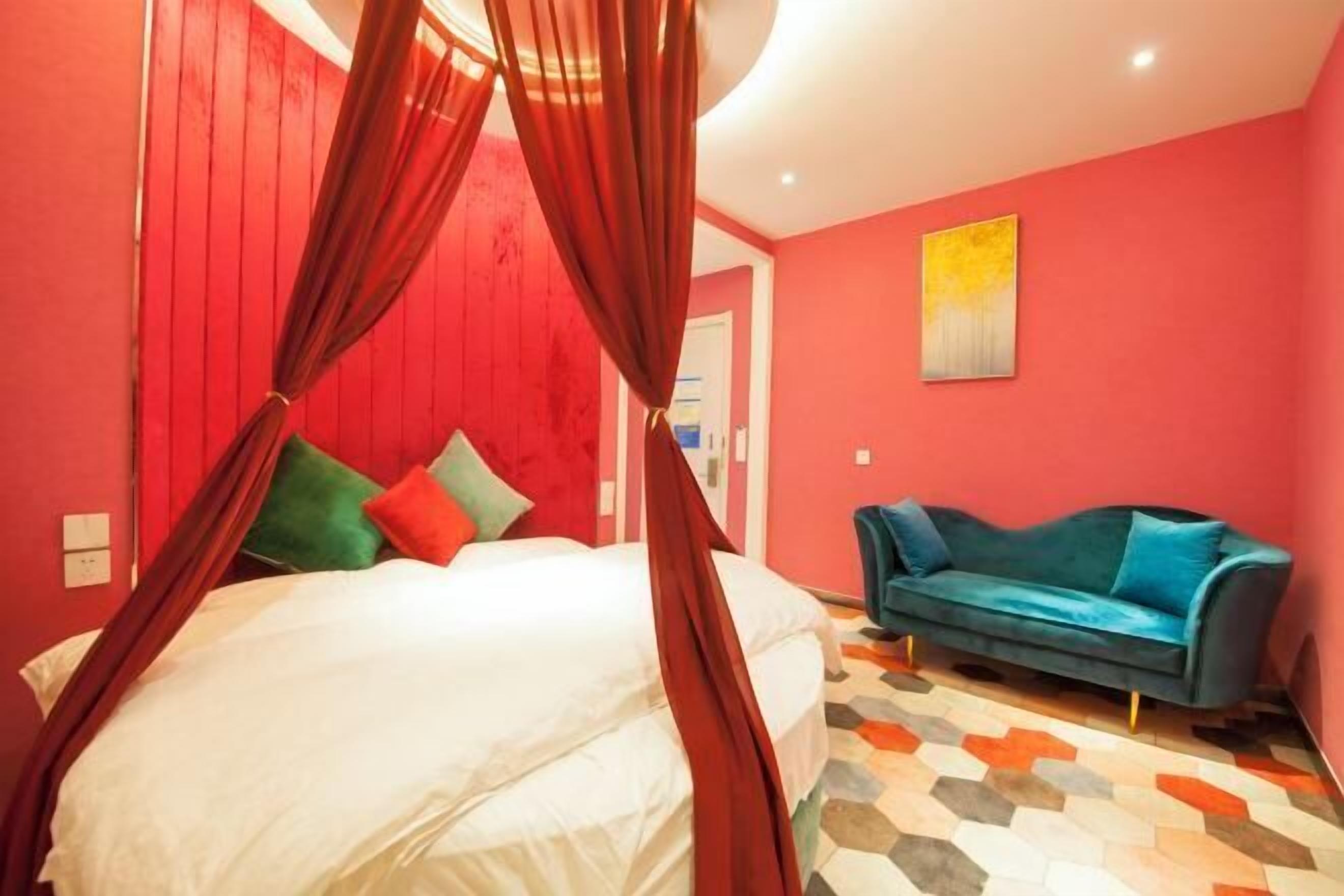 A bedroom with a canopy bed, a teal sofa, and a geometric patterned floor.