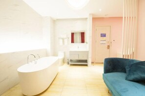 A modern bathroom with a freestanding bathtub, a vanity with a mirror, and a blue sofa.
