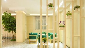 A room with a large potted plant, green upholstered chairs, a small table, and a white partition with plants. - Yuxi Zhuoran Xinzhuang Hotel (Yuxi)
