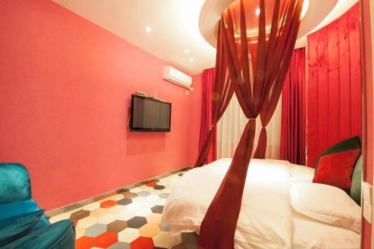 A bedroom with a bed, red curtains, a television, and a hexagonal patterned floor.