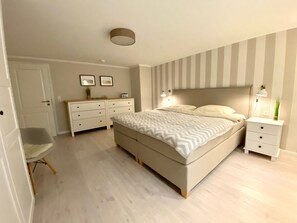 Ein Schlafzimmer mit Bett, Nachttischen, einem Schminktisch und einem Sessel.