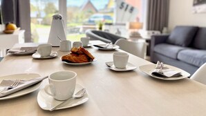 A dining table set with plates, cups, and cutlery in a modern room with a sofa and a view of houses.