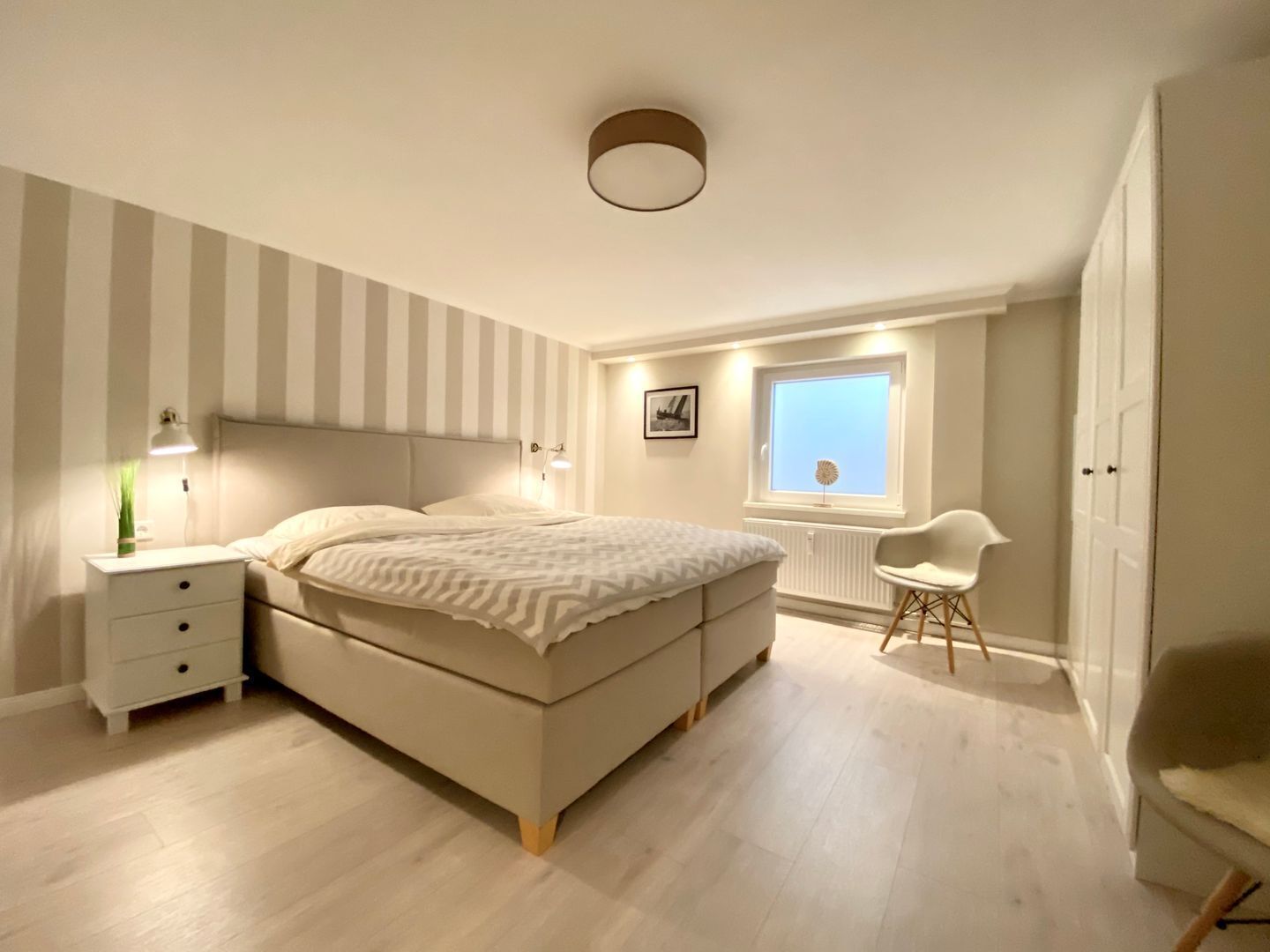 A bedroom with a bed, bedside tables, a chair, a window, and a radiator.