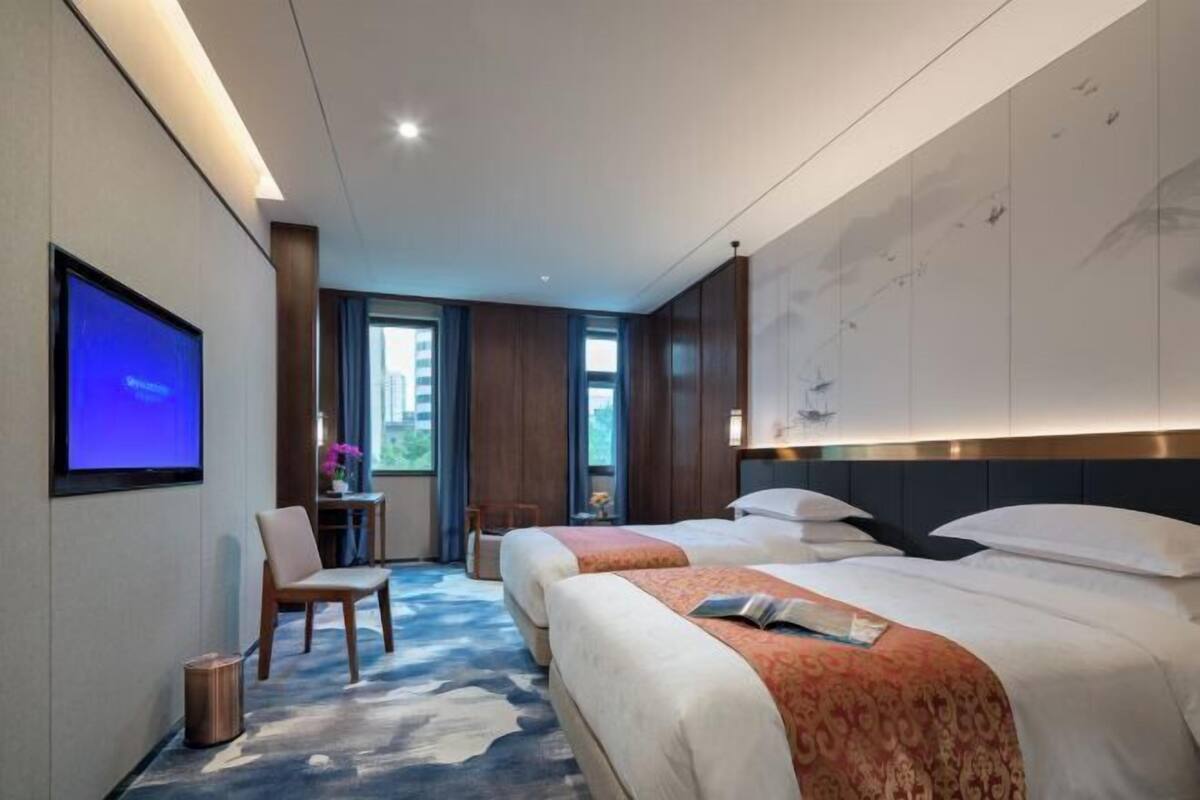 A hotel room with two beds, a television, a desk, and a chair.