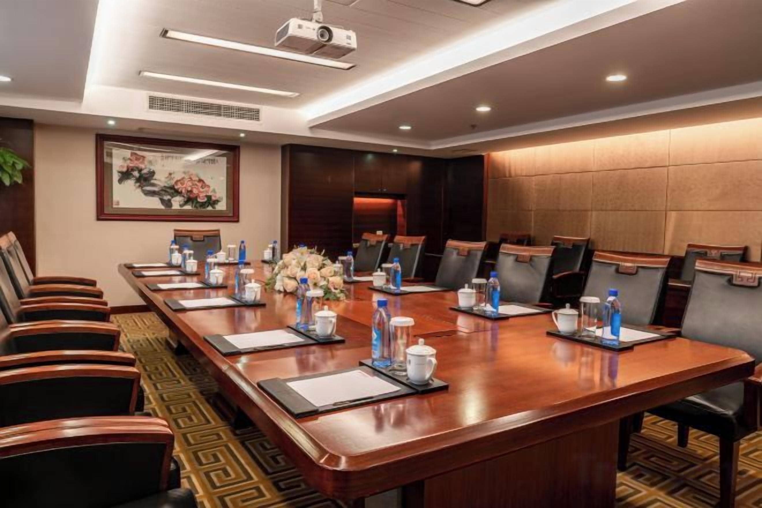 Un salón de conferencias con una larga mesa, sillas, un proyector y un arreglo floral.