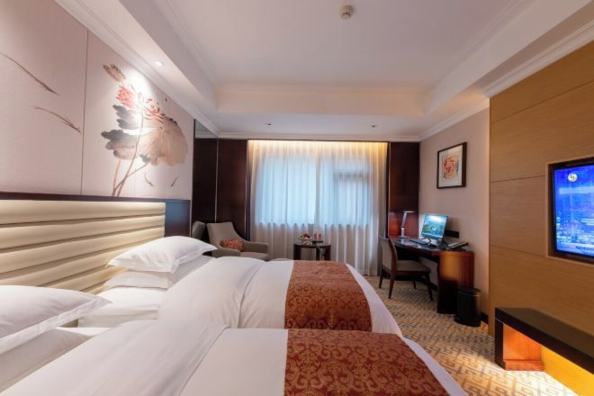 A hotel room with a bed, a desk, a television, and a window with curtains.