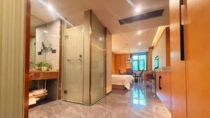 Een hotelkamer met een bed, een bureau, een spiegel en een badkamer met douche en wastafel.