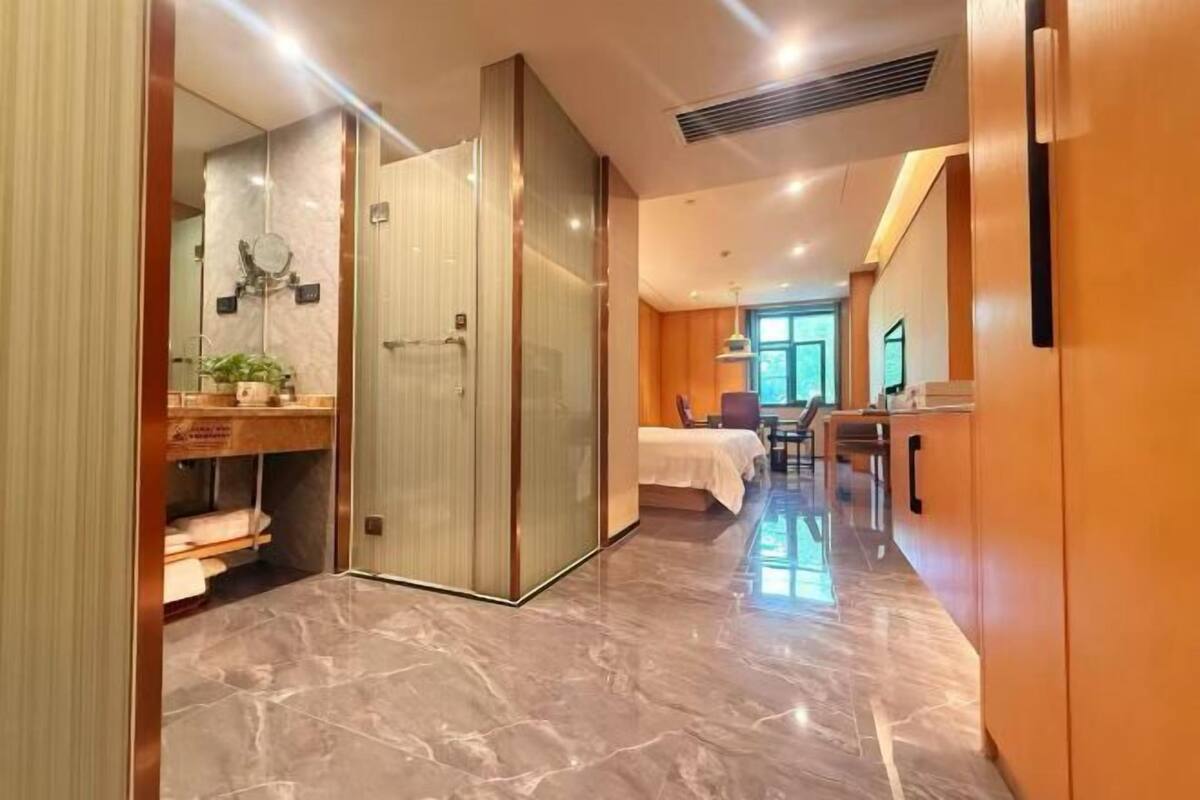 A hotel room with a bed, a desk, a mirror, and a bathroom with a shower and sink.