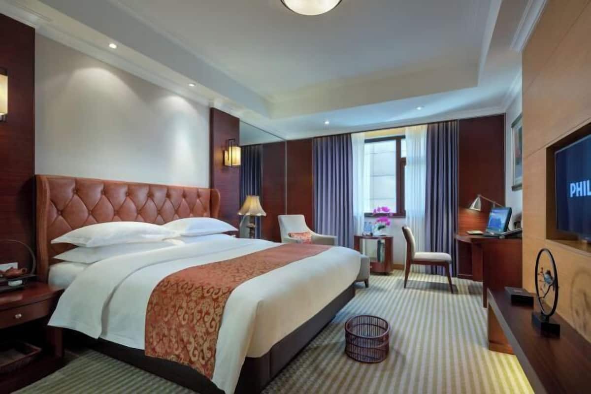 A hotel room with a large bed, a desk with a computer, a chair, and a TV.