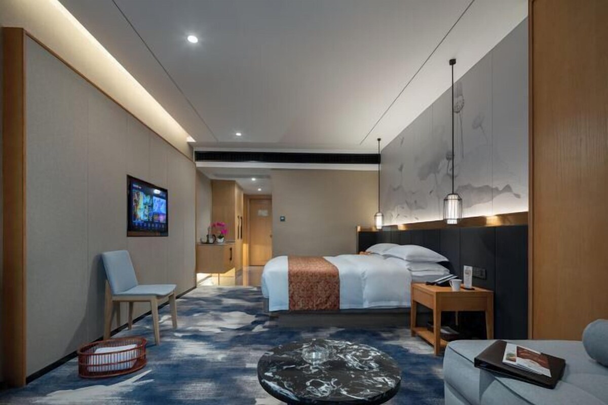 Une chambre d’hôtel comprenant un lit, un coin salon, une télévision et une œuvre d’art accrochée au mur.
